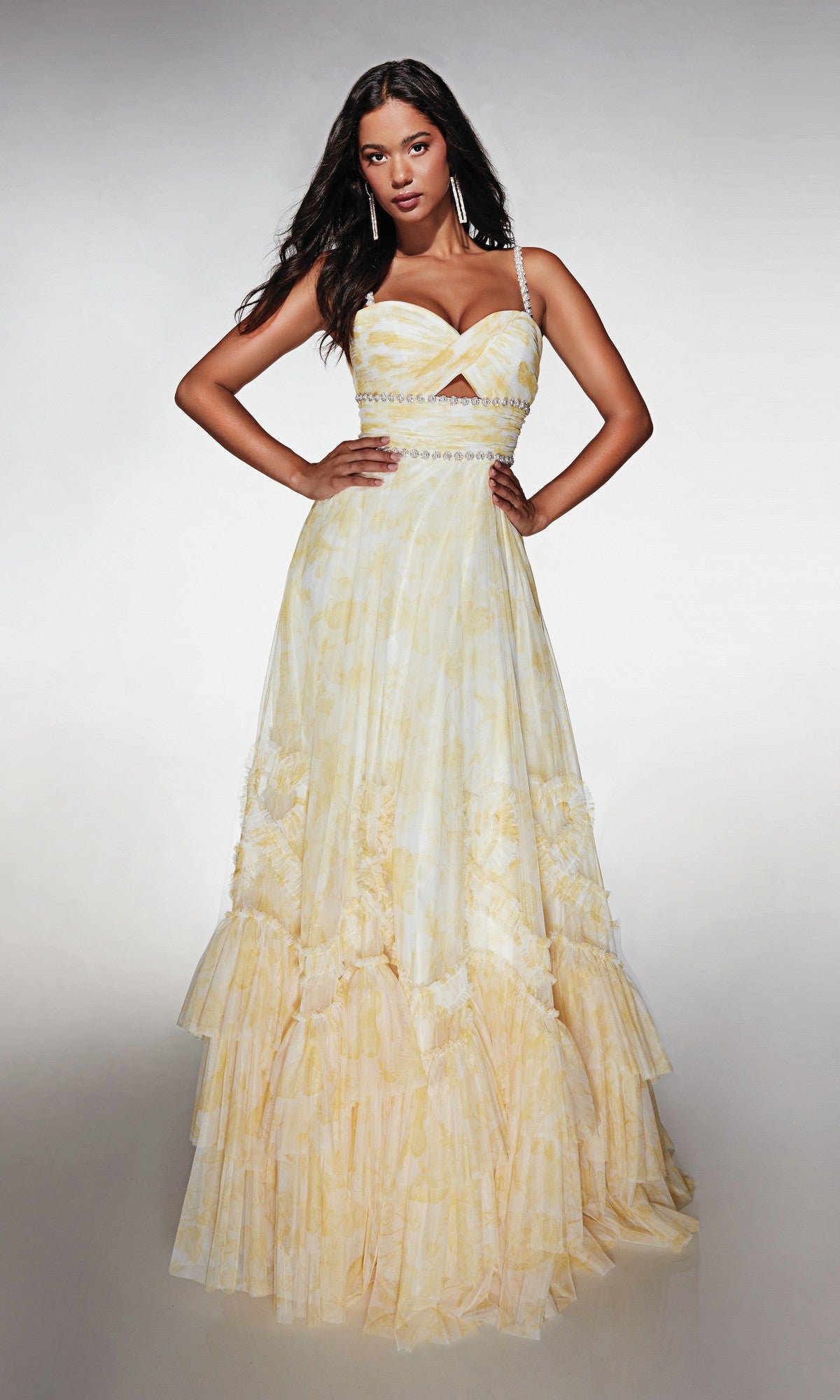 A woman stands with hands on hips, wearing the Alyce 62063 long formal dress featuring a strapless yellow design with ruffles and a fitted, embellished bodice against a plain background.